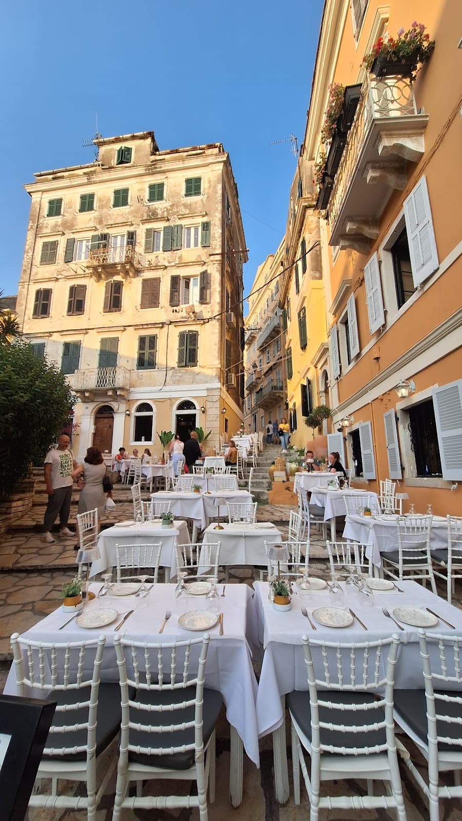 Daytime terrace with white tables set in Corfu's old town lane