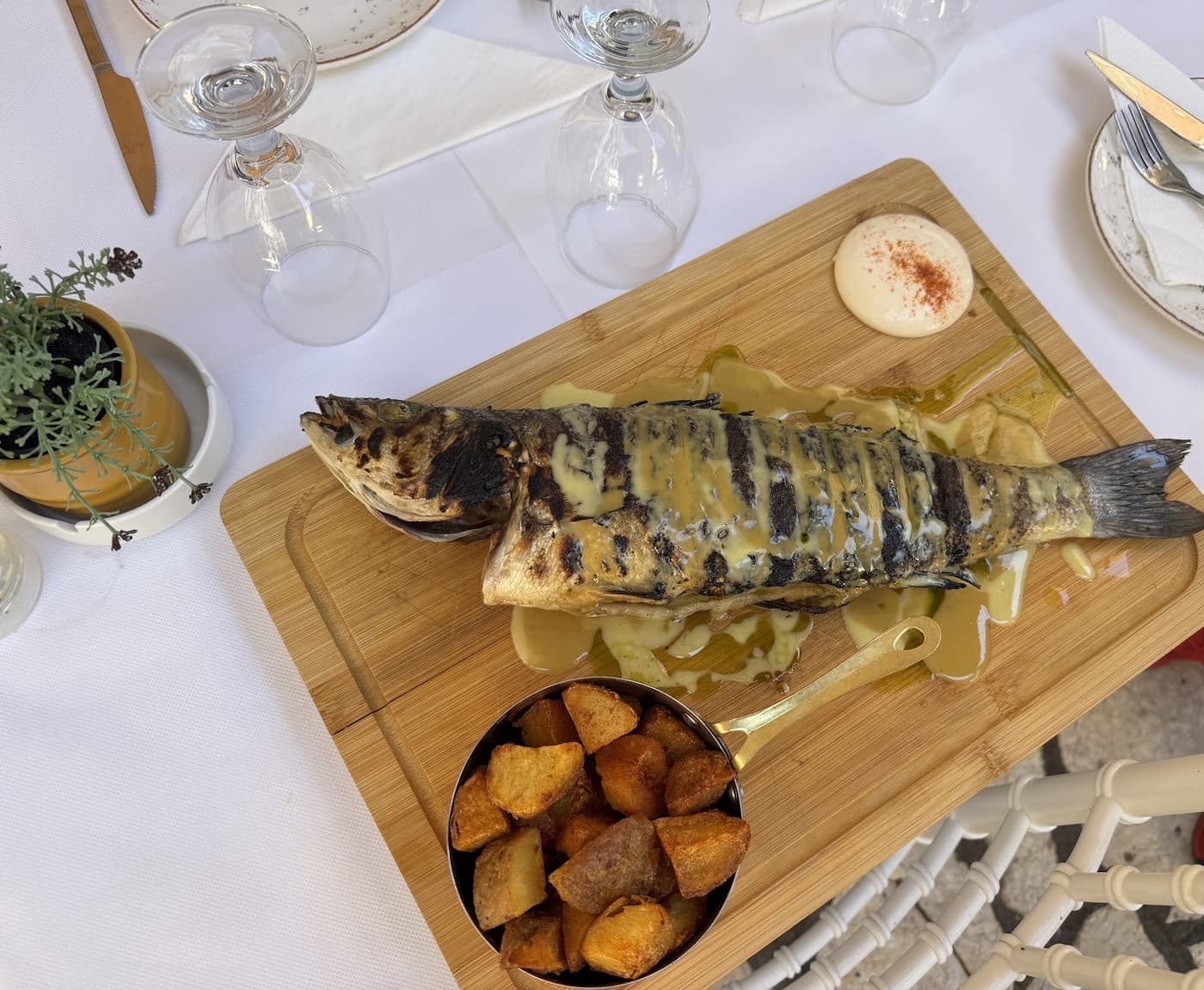 Whole grilled sea bass on a wooden board with roasted potatoes